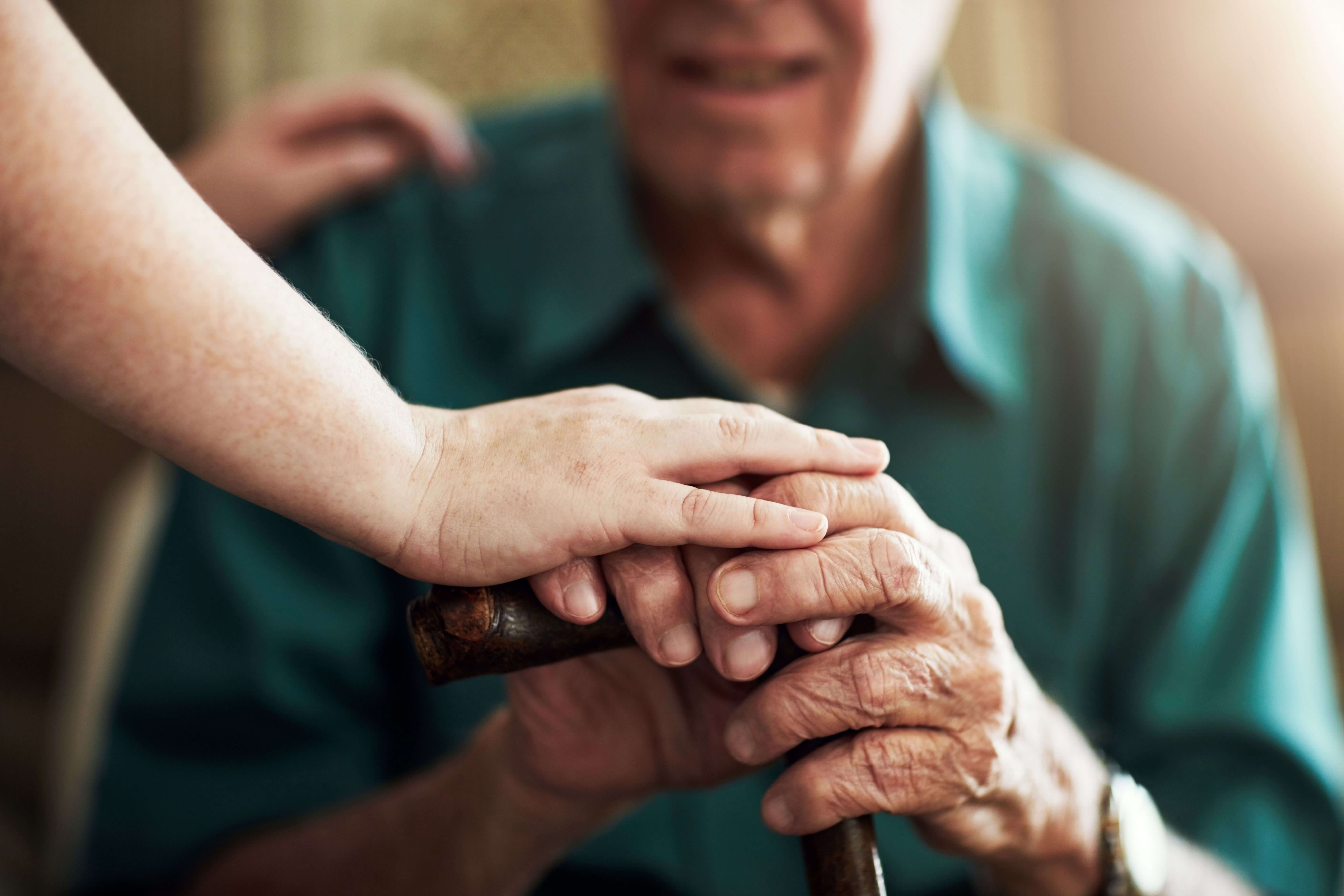 Close up of caregivers hand on top of seniors hands, while they hold their cane.