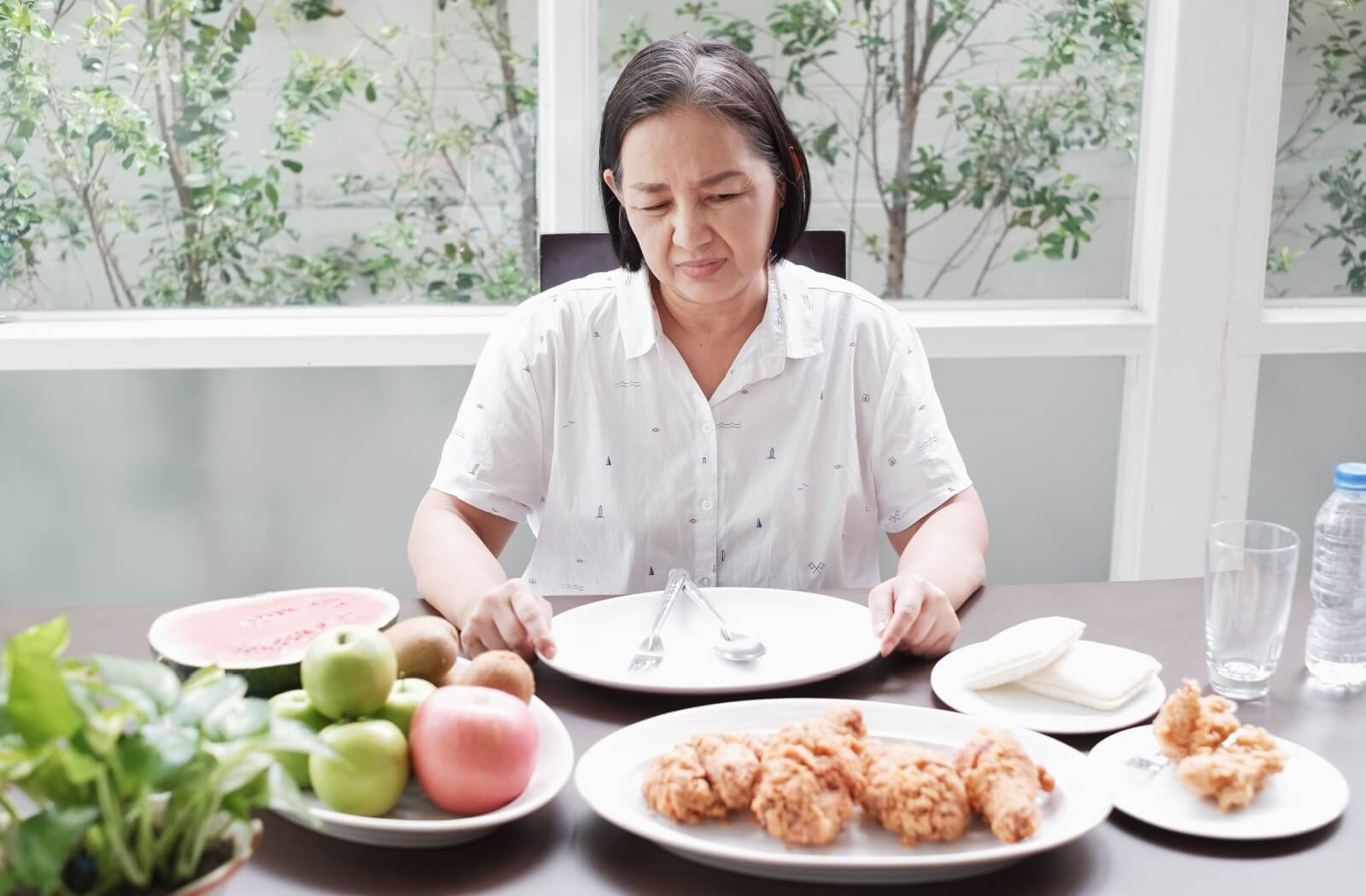 A senior with dementia looks in distaste at different foods offered for mealtime; however, their plate remains empty