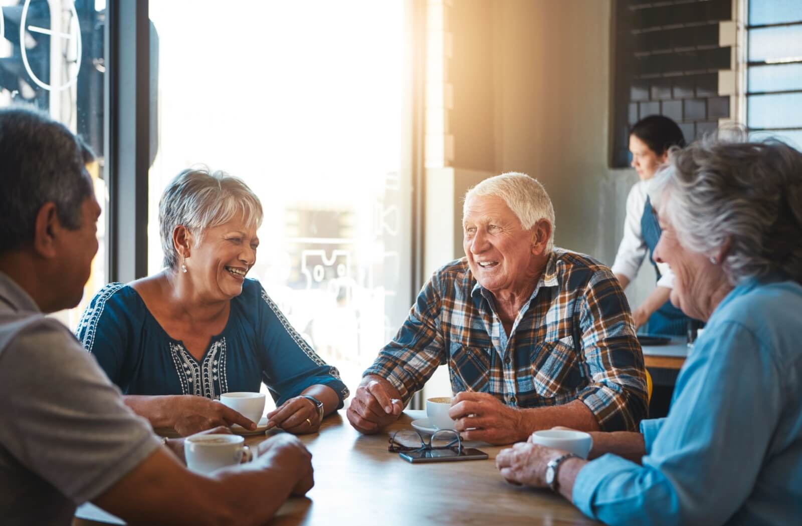Senior friends relax at a cafe, holding coffee cups while chatting and laughing.