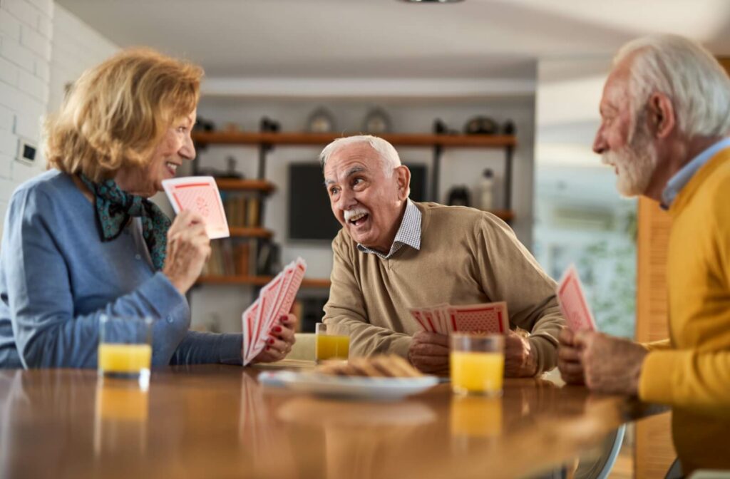 A group of older adults laughing and playing cards at the table in assisted living.