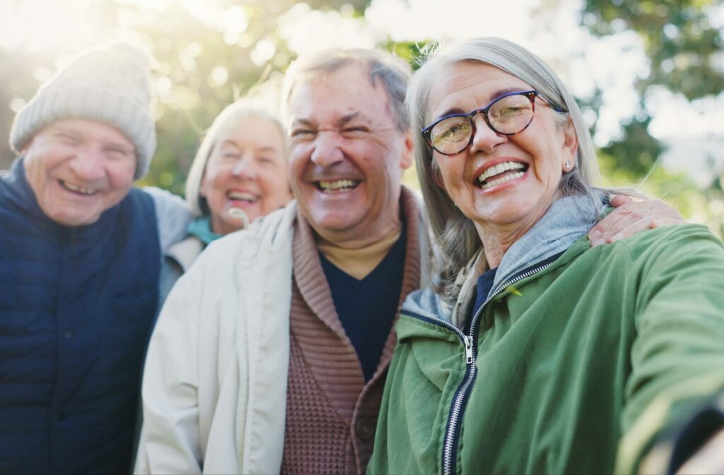 Senior friends taking a group selfie in a park, while smiling at the phone.