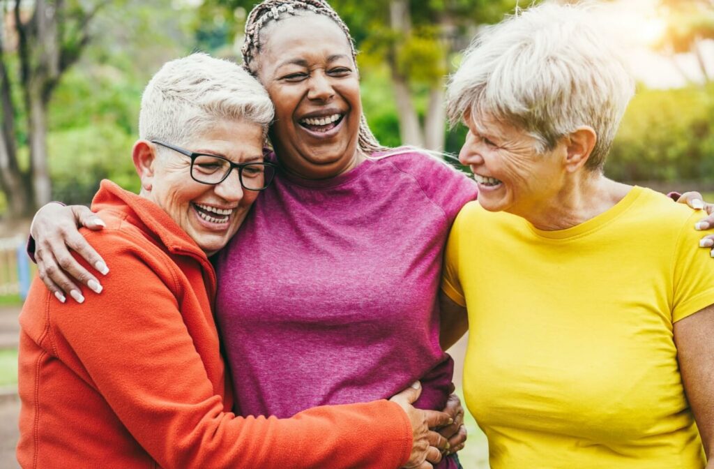 three senior women holding each other and enjoying social life after downsizing to a senior living community