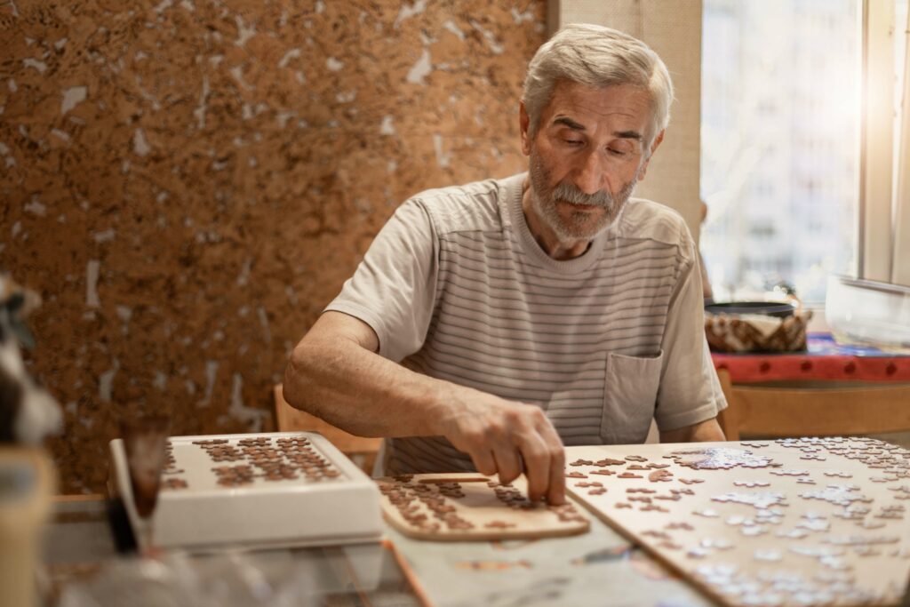 An older man sitting at a table working on a jigsaw puzzle.