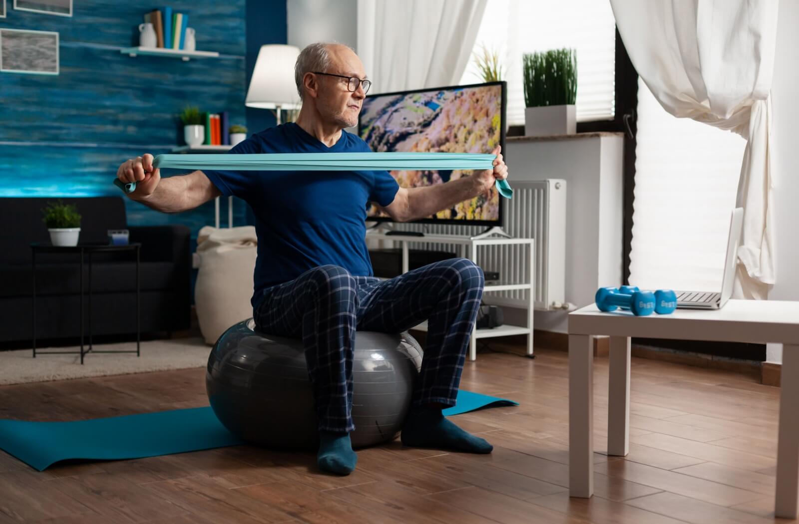 senior doing exercises at home with pilates ball and resistance band